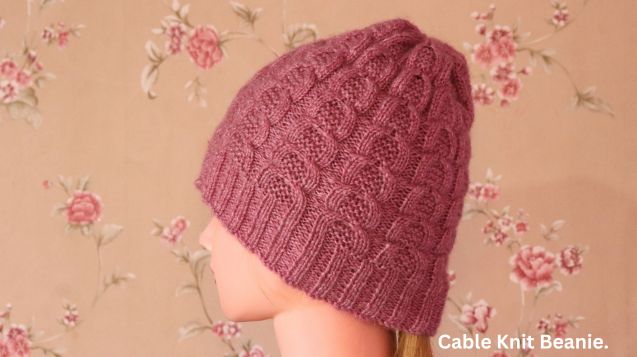 A mannequin head showcases the Sunayana's Cable Knit Beanie, with a colorful floral design in the background.